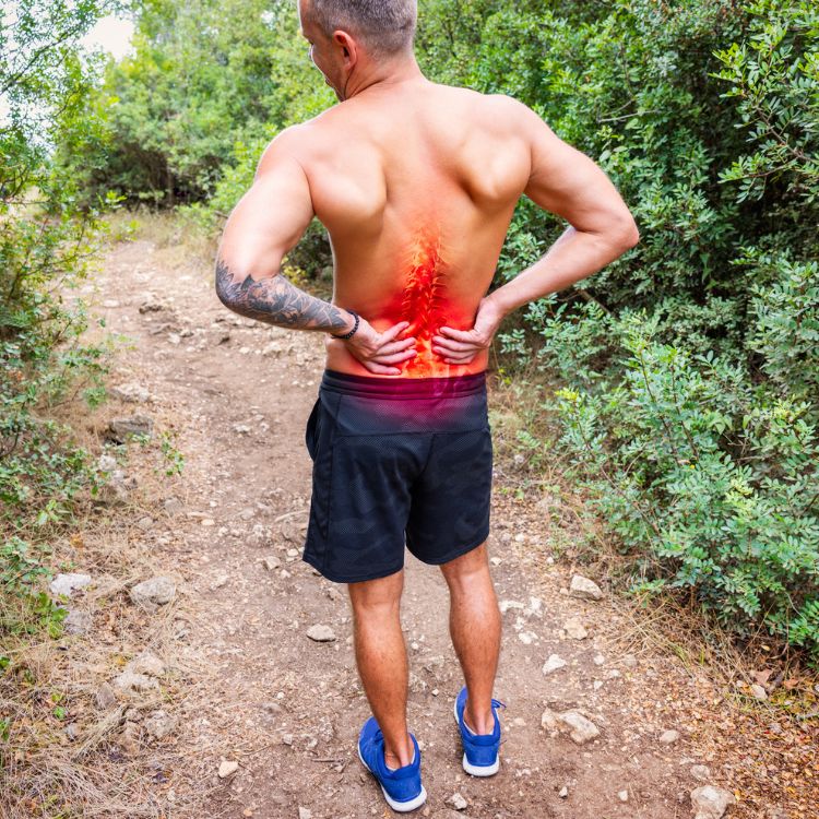 A man outside exercising, holding on to his lower back in pain.